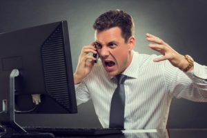 Angry businessman yelling at an IT helpdesk person on the phone in front of a broken desktop computer. 