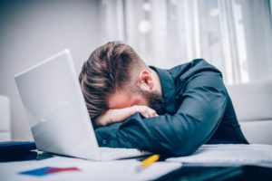 Small business owner upset over being hacked in the workplace. Leaning head on crossed arms over a laptop 