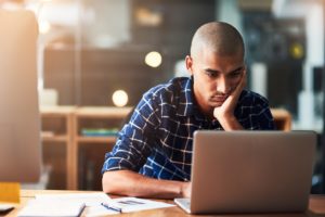 Man waiting on a slow running website at a desk on a laptop 