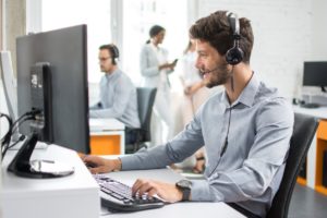 Smiling handsome customer support operator agent making VOIP calls on a nice headset with a good quality microphone with hands-free device working in call center