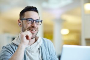 Portrait of contemporary adult man smiling while using laptop to video call using VoIP 