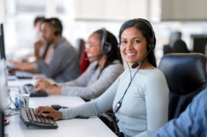 Confident female operator with a headset is working with colleagues at desk in an IT help desk call center