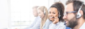 Call center worker accompanied by her team. Smiling customer support operator at work. Young employee working with a headset.