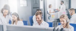  IT help desk worker accompanied by his team. Smiling customer support operator at work. Young employee working with a headset. 