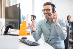 A happy male technical support operator working in an IT help desk call center setting speaking and assisting a customer online and speaking through a headset. 