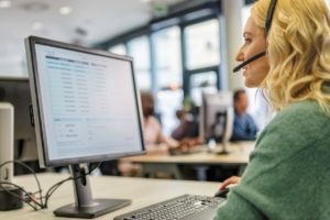 Woman working in a call center live help desk using a headset and computer to attend to calls. 