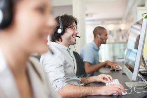 Diverse group of employees with headsets working at computers in an office. 