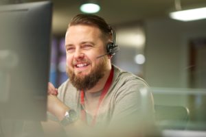 Employee working for a company's live answer help desk, wearing a headset to answer calls and solve client's IT issues. 