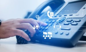 Employee's hand pressing a button on a company phone system - showing different features of using VoIP. 